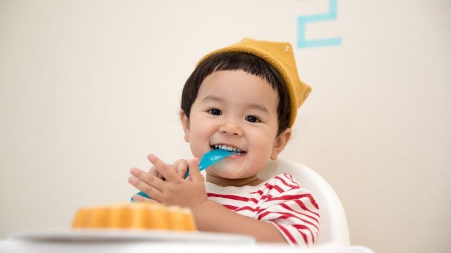 asian toddler in a highchair wearing a party hat