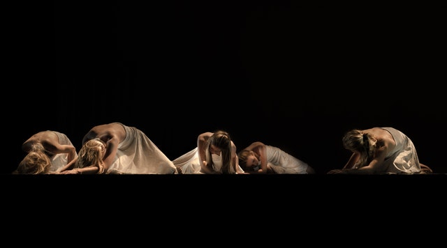 Five girls lie on stage during a drama performance.