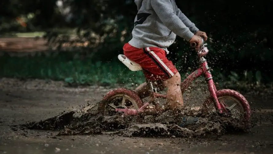 Photo of a young boy riding a balance bike through a muddy puddle