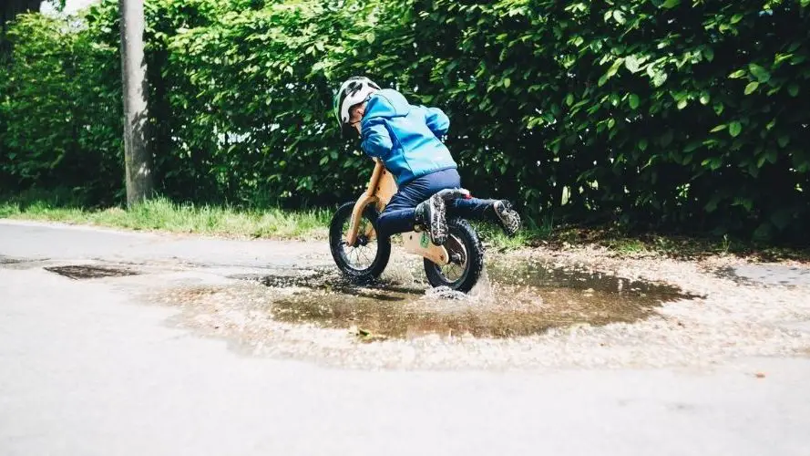 Photo of a boy riding a balance bike through a puddle